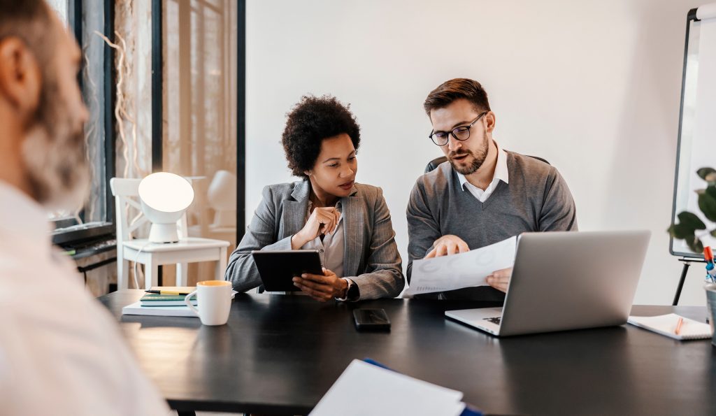 Selective focus on businesspeople sitting at the corporate firm and looking at the solution about project while an executive sitting across them at the table in blurry foreground.